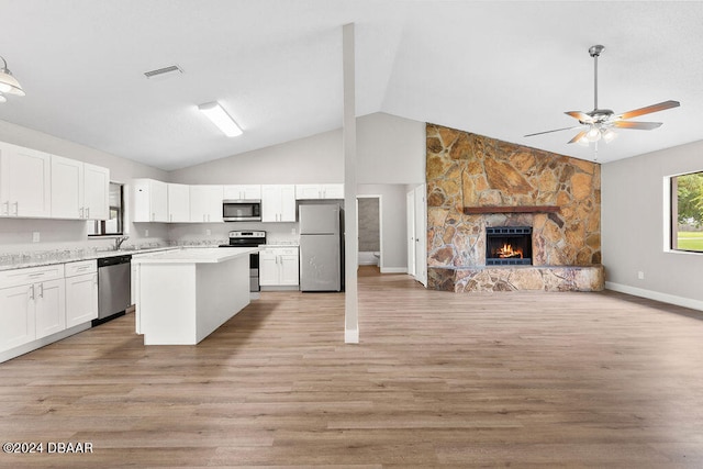 kitchen featuring stainless steel appliances, a stone fireplace, light wood-type flooring, white cabinets, and lofted ceiling