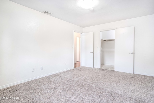 unfurnished bedroom with light colored carpet, a closet, and a spacious closet