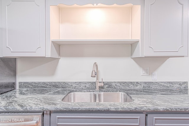 kitchen with white cabinetry, sink, and light stone countertops