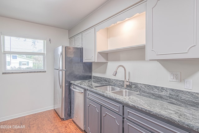 kitchen with light hardwood / wood-style floors, dark stone counters, sink, gray cabinetry, and stainless steel dishwasher