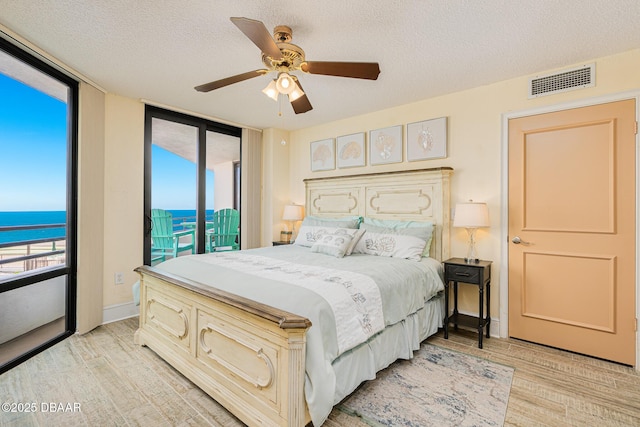 bedroom featuring light wood-type flooring, a textured ceiling, access to outside, ceiling fan, and a water view