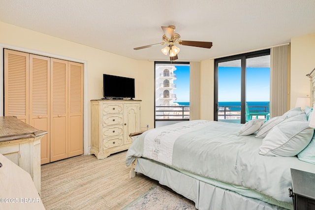 bedroom featuring access to outside, ceiling fan, a wall of windows, light hardwood / wood-style floors, and a closet