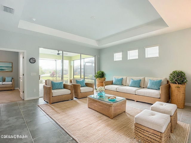 tiled living room featuring a raised ceiling, plenty of natural light, and ceiling fan