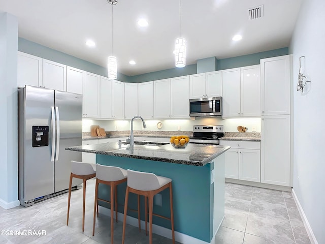 kitchen with white cabinets, appliances with stainless steel finishes, a kitchen island with sink, and sink