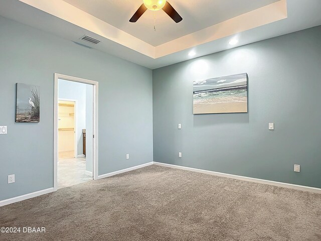 empty room featuring a raised ceiling, ceiling fan, and carpet floors