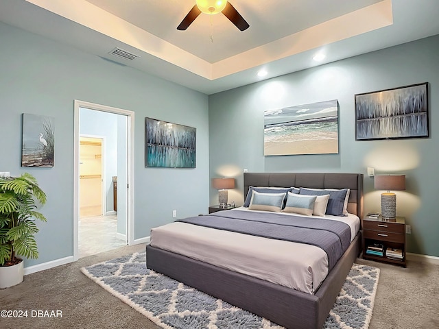 bedroom featuring a raised ceiling, connected bathroom, ceiling fan, and carpet