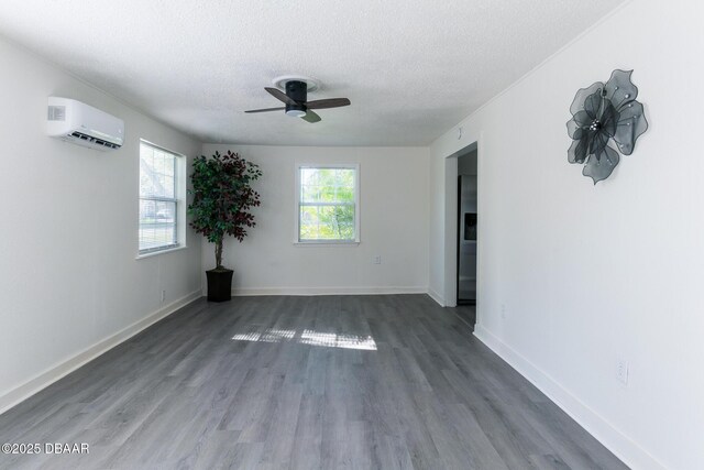 empty room with a textured ceiling, a healthy amount of sunlight, an AC wall unit, and dark wood-type flooring