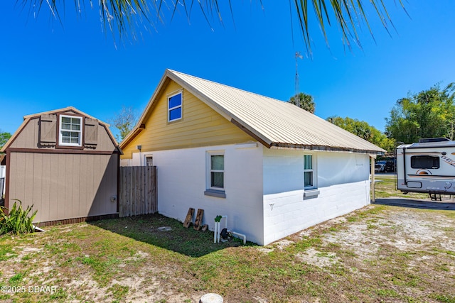 view of property exterior with fence, concrete block siding, metal roof, an outbuilding, and a storage unit