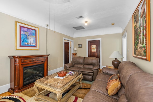 living room featuring a glass covered fireplace, visible vents, baseboards, and wood finished floors