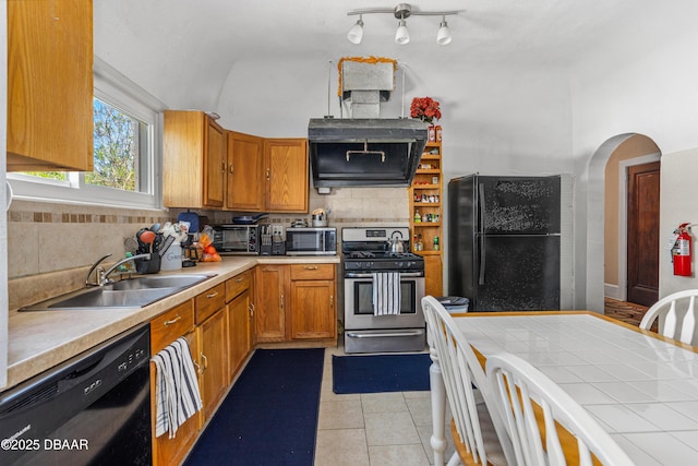 kitchen featuring brown cabinets, black appliances, a sink, light tile patterned floors, and decorative backsplash