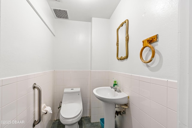 half bath featuring tile walls, toilet, and wainscoting