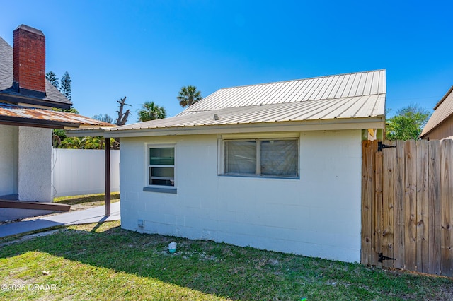 view of side of property with metal roof, concrete block siding, and fence