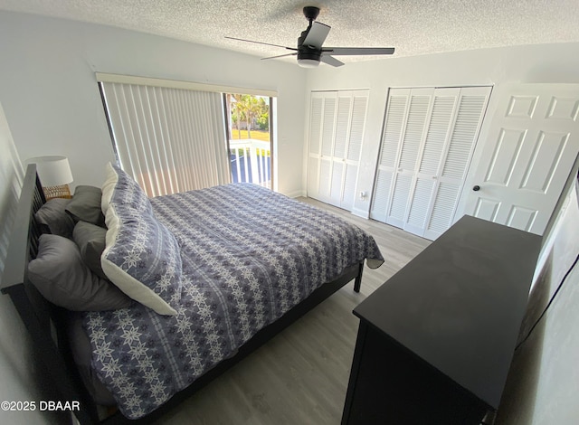 bedroom featuring hardwood / wood-style flooring, ceiling fan, multiple closets, and a textured ceiling