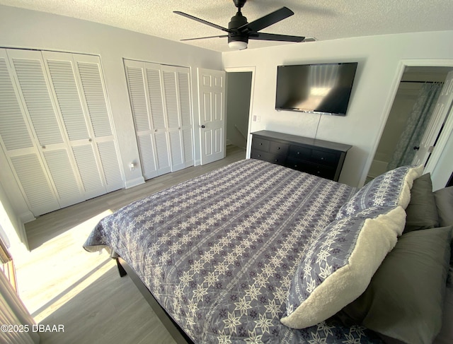 bedroom with ceiling fan, a textured ceiling, wood-type flooring, and multiple closets