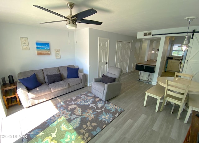 living room featuring ceiling fan, a barn door, and light hardwood / wood-style flooring