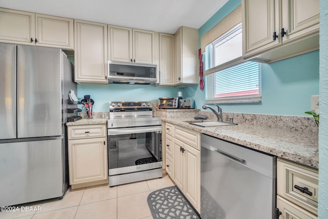 kitchen with sink, light stone counters, cream cabinets, light tile patterned floors, and appliances with stainless steel finishes