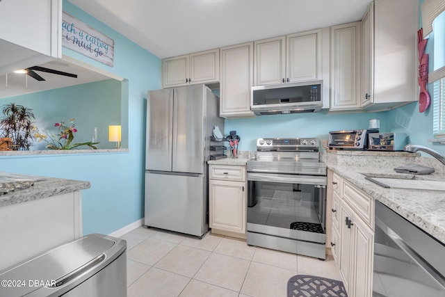 kitchen with light stone counters, sink, light tile patterned floors, and stainless steel appliances