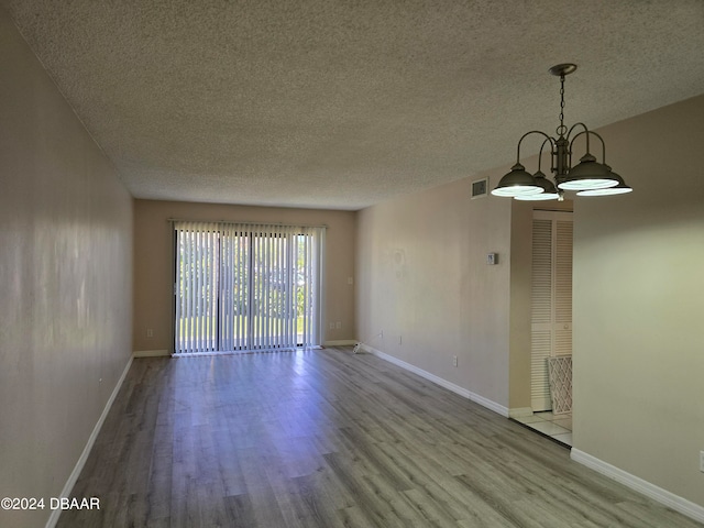 spare room featuring light hardwood / wood-style floors, a textured ceiling, and an inviting chandelier