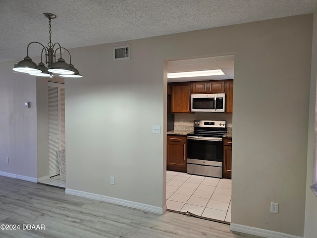 kitchen with stainless steel appliances, a textured ceiling, decorative light fixtures, an inviting chandelier, and light hardwood / wood-style floors