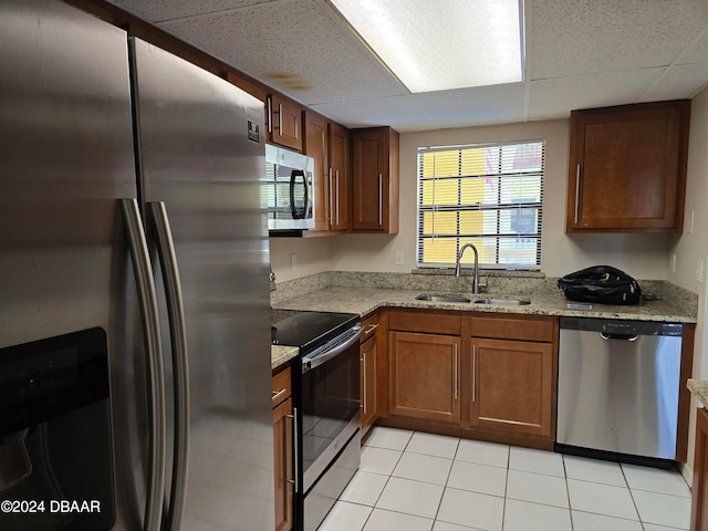 kitchen with appliances with stainless steel finishes, sink, light stone counters, and light tile patterned floors