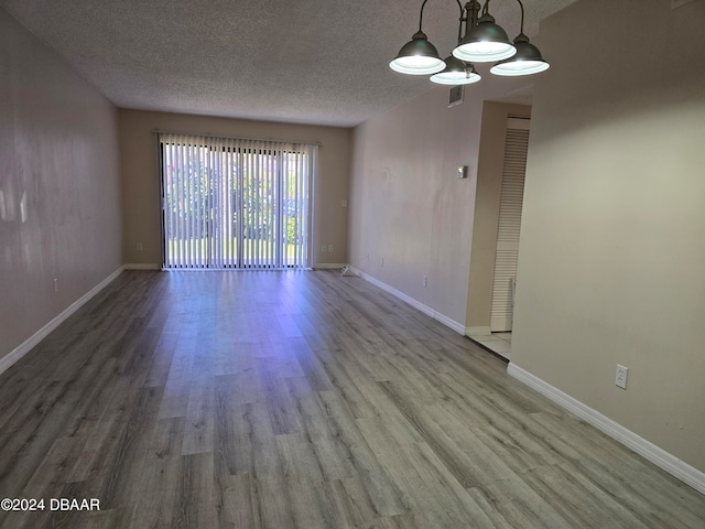 empty room with hardwood / wood-style flooring, a chandelier, and a textured ceiling