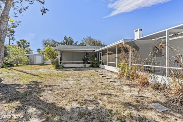 rear view of property with a storage unit, an outdoor structure, a chimney, and a sunroom