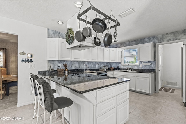 kitchen featuring a sink, dark stone counters, white cabinets, and light tile patterned floors