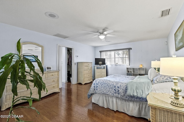 bedroom with a walk in closet, wood finished floors, visible vents, and ceiling fan