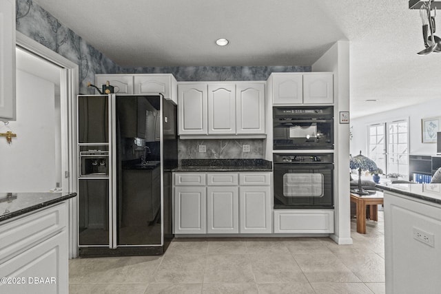 kitchen with dark stone counters, light tile patterned flooring, black appliances, white cabinets, and a textured ceiling