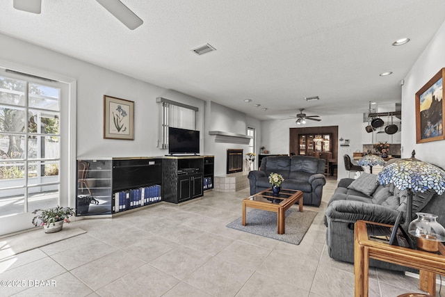 living room featuring light tile patterned floors, visible vents, a fireplace, and a ceiling fan