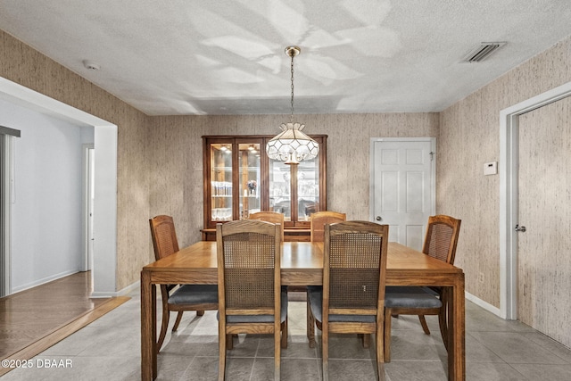 dining space with visible vents, baseboards, a textured ceiling, and wallpapered walls