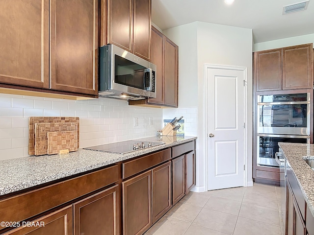 kitchen featuring visible vents, light stone counters, appliances with stainless steel finishes, light tile patterned flooring, and decorative backsplash