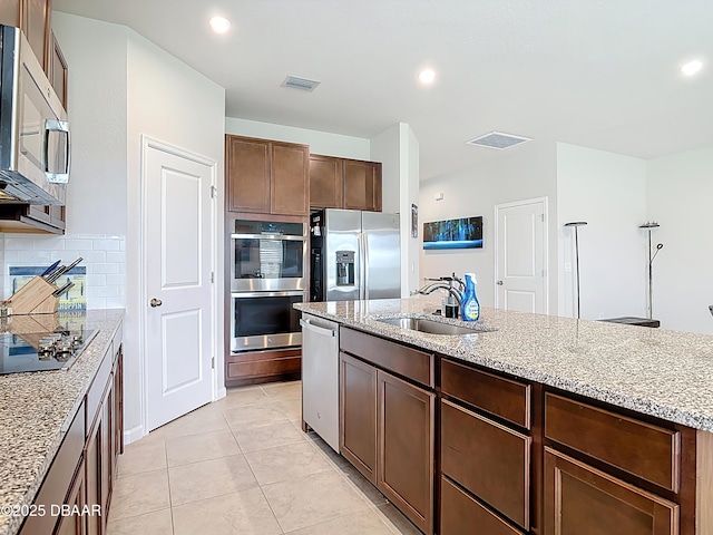 kitchen featuring tasteful backsplash, light stone countertops, light tile patterned floors, stainless steel appliances, and a sink