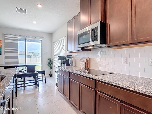 kitchen featuring visible vents, stainless steel microwave, decorative backsplash, black electric stovetop, and light stone countertops