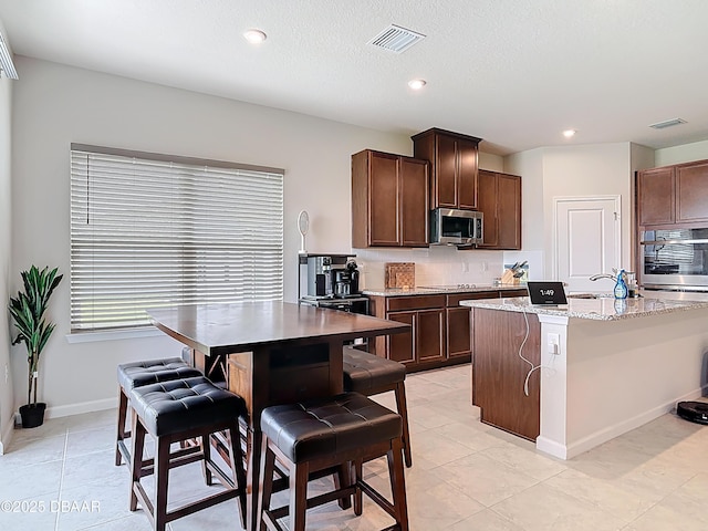 kitchen with light stone counters, stainless steel appliances, visible vents, and decorative backsplash