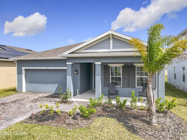 ranch-style home with covered porch, stucco siding, an attached garage, and decorative driveway