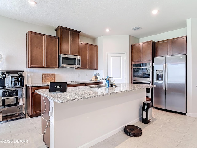 kitchen with tasteful backsplash, visible vents, light stone countertops, stainless steel appliances, and a sink