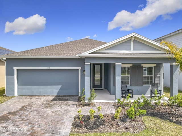 view of front of house with decorative driveway, covered porch, an attached garage, and stucco siding