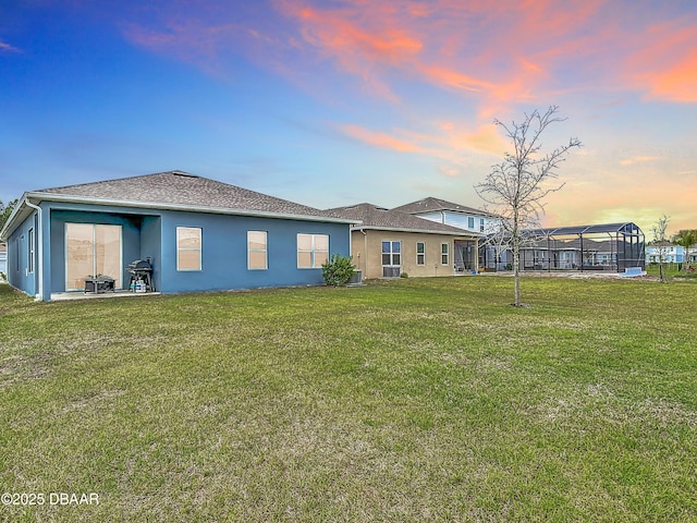 back of property at dusk featuring stucco siding, a yard, and a shingled roof