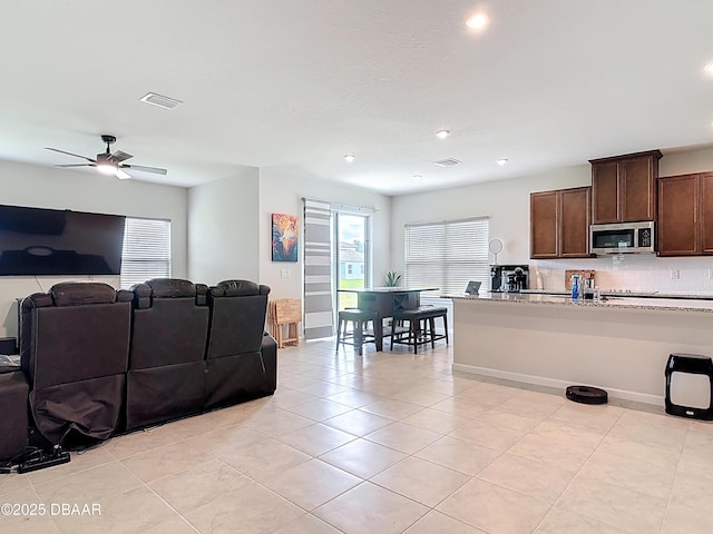 living room with light tile patterned flooring, visible vents, baseboards, and a ceiling fan