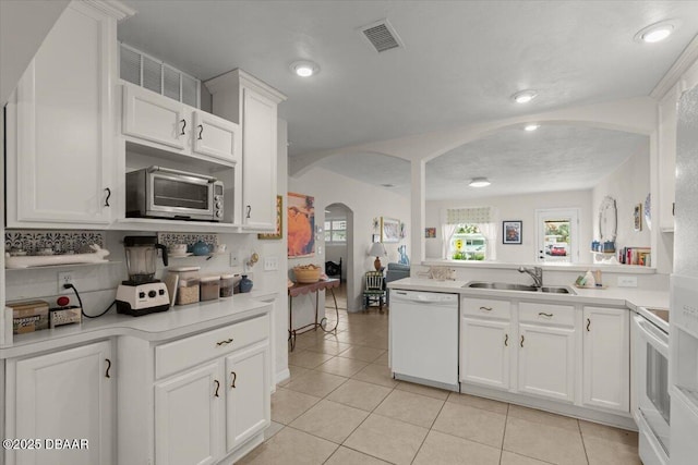 kitchen with tasteful backsplash, sink, white appliances, white cabinetry, and light tile patterned floors