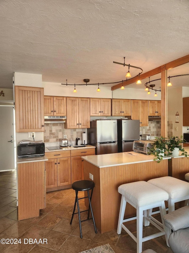 kitchen with a kitchen bar, decorative backsplash, stainless steel refrigerator, and rail lighting