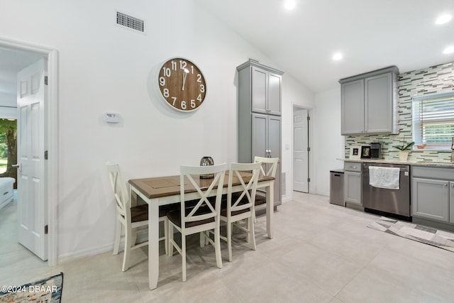 kitchen featuring decorative backsplash, gray cabinetry, stainless steel dishwasher, and vaulted ceiling