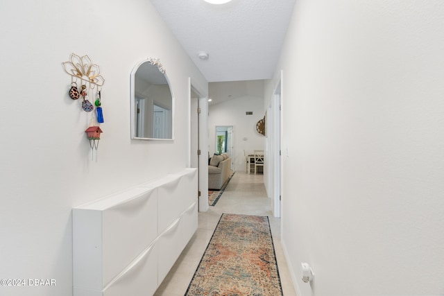 corridor featuring lofted ceiling, a textured ceiling, and light tile patterned floors