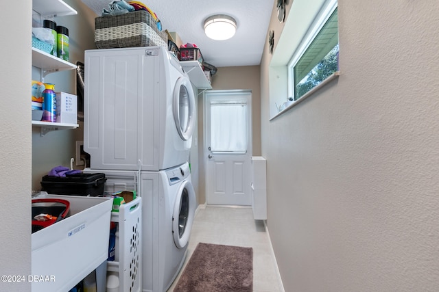 laundry area featuring a textured ceiling, stacked washer / dryer, and sink