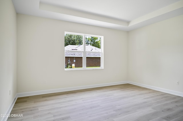 spare room featuring a tray ceiling and light hardwood / wood-style floors