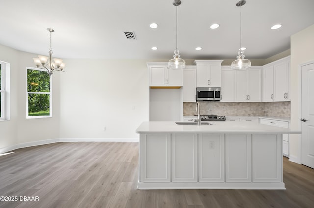 kitchen featuring decorative backsplash, white cabinetry, an inviting chandelier, and an island with sink