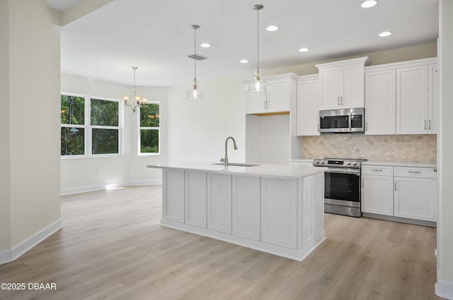 kitchen featuring sink, hanging light fixtures, a kitchen island with sink, stainless steel appliances, and white cabinets