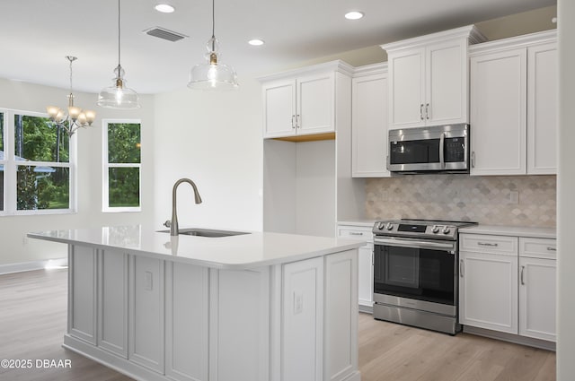 kitchen with white cabinets, appliances with stainless steel finishes, decorative light fixtures, sink, and a kitchen island with sink