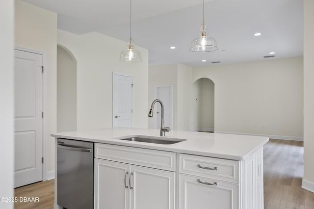 kitchen with decorative light fixtures, stainless steel dishwasher, sink, white cabinetry, and an island with sink